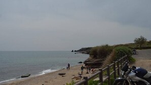 Une plage avec une clôture en bois, une moto garée et des personnes se promenant le long du rivage.