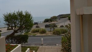 Une vue sur la côte, aperçue à travers une porte, avec un sentier pavé, une moto garée et un arbre.