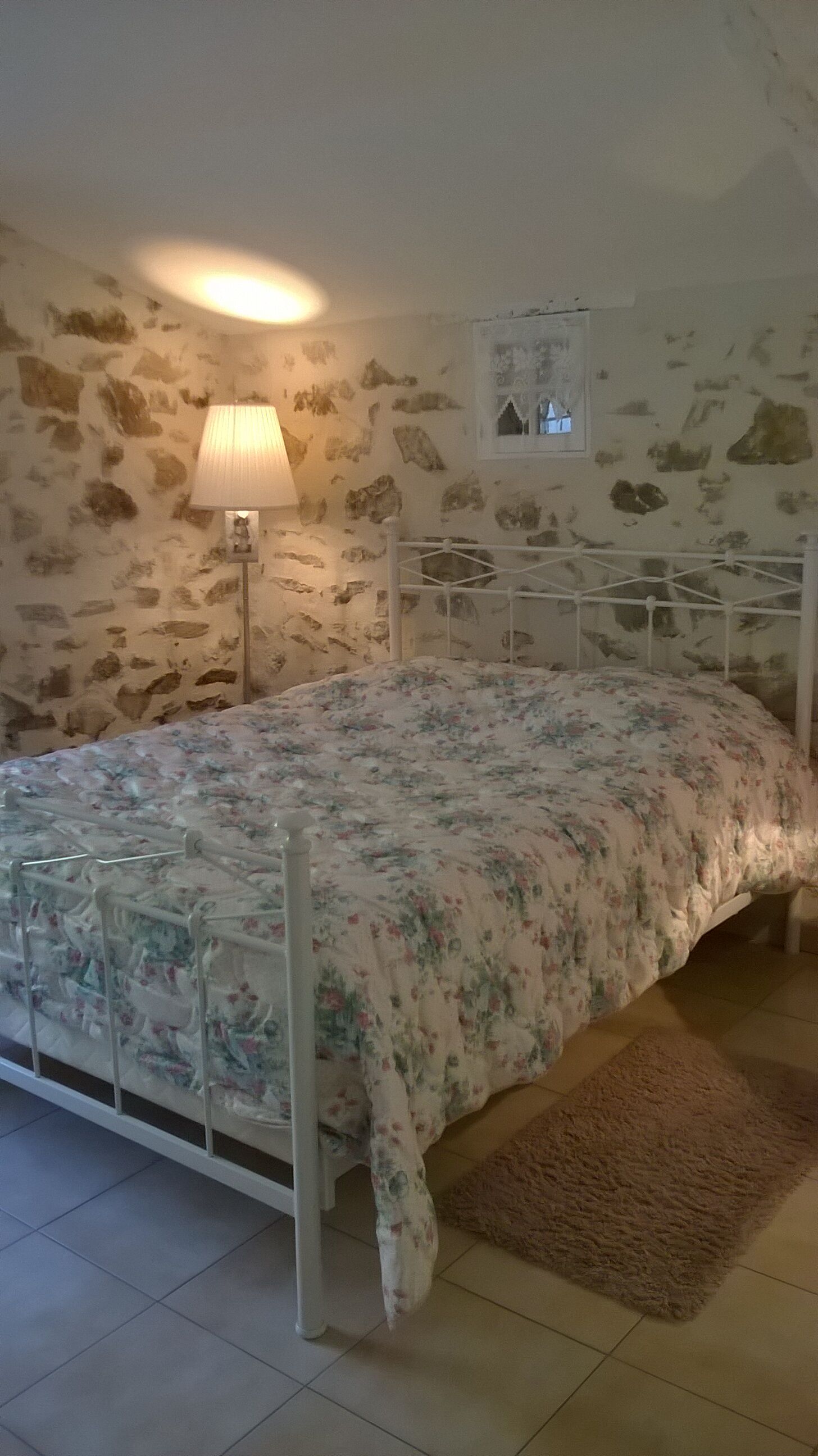 A bedroom with a bed, a lamp, a stone wall, and a small window.