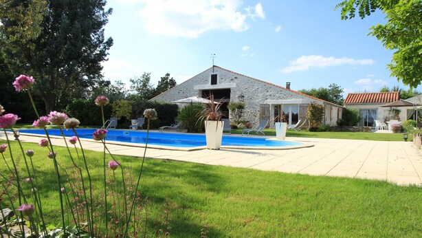 Une maison avec une piscine, une façade en pierre et une pelouse.