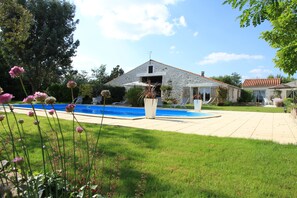 Et hus med swimmingpool, stenvæg og græsplæne.