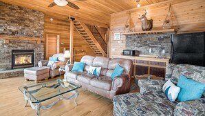 A cozy living room with a stone fireplace, leather sofas, a glass coffee table, and a wooden ceiling.