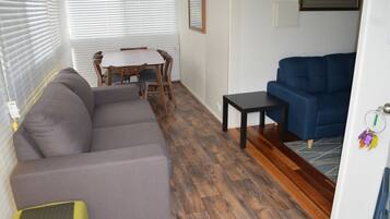 A living room with a gray sofa, a blue couch, a wooden dining table with chairs, and a small black table.