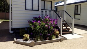 A mobile home with a covered porch and a small garden with purple flowers.
