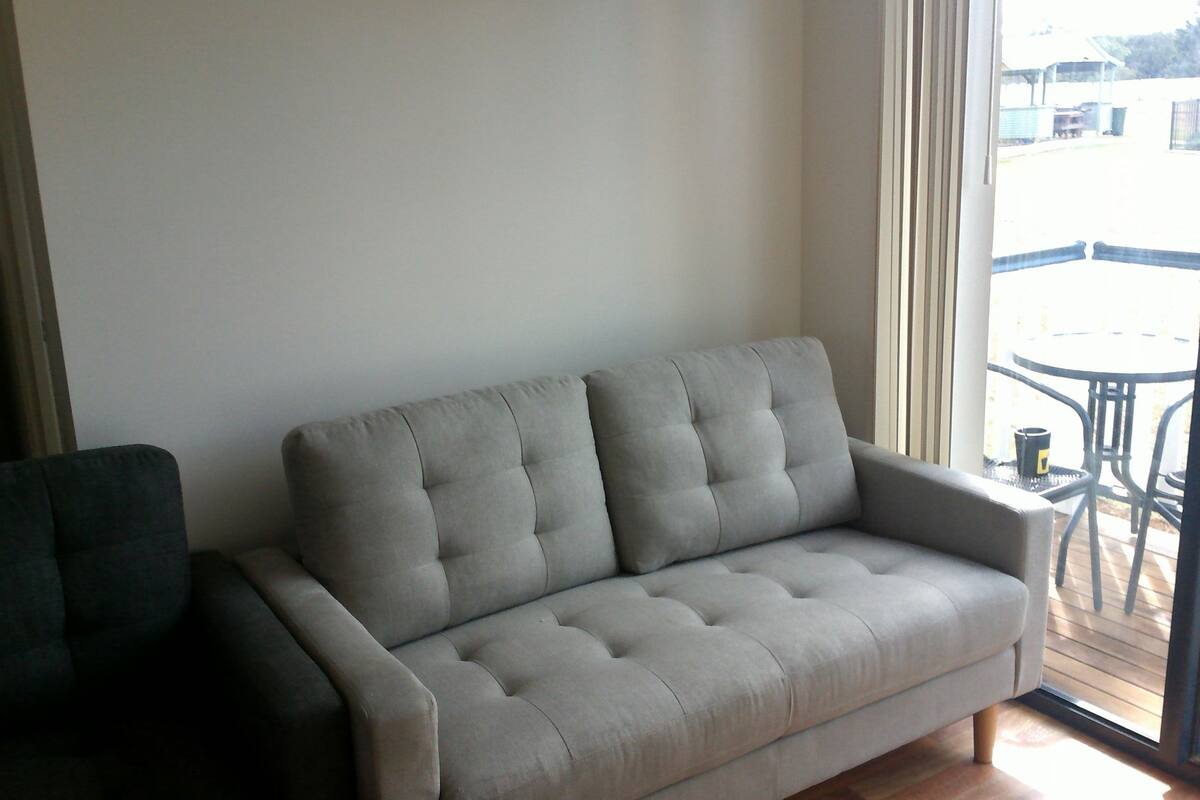 Un sofá gris en una habitación con un ventanal grande, una mesita y una silla.