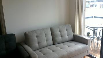 A grey sofa in a room with a large window, a small table, and a chair.