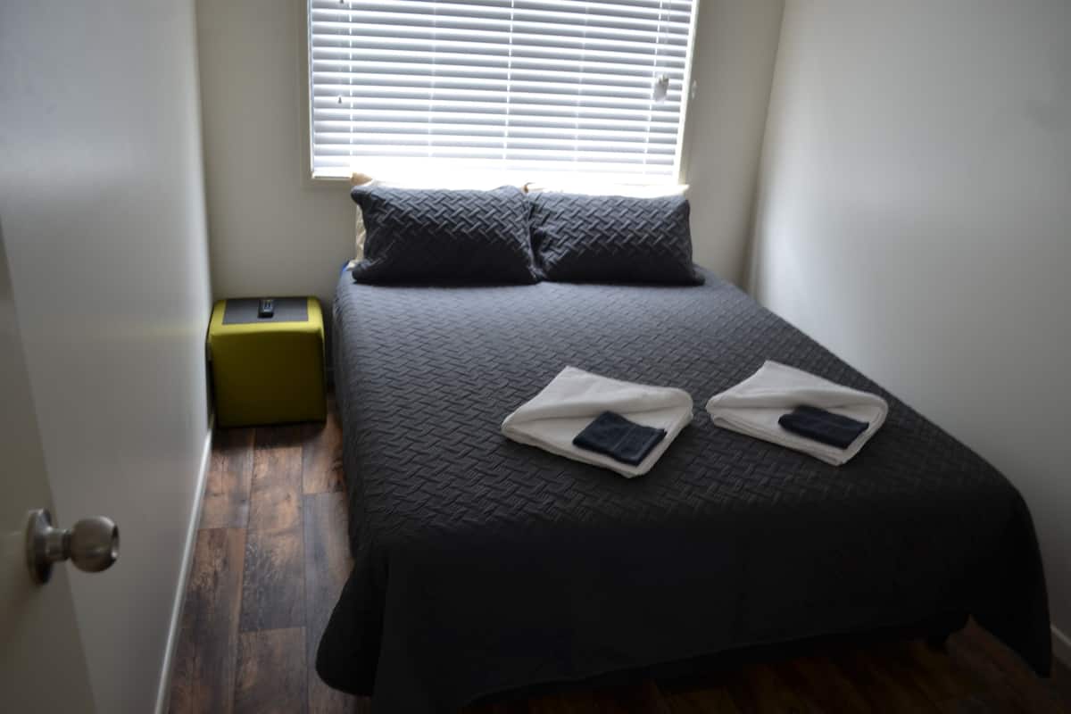 Una cama bien hecha con un edredón oscuro, dos almohadas y dos toallas dobladas sobre la cama.