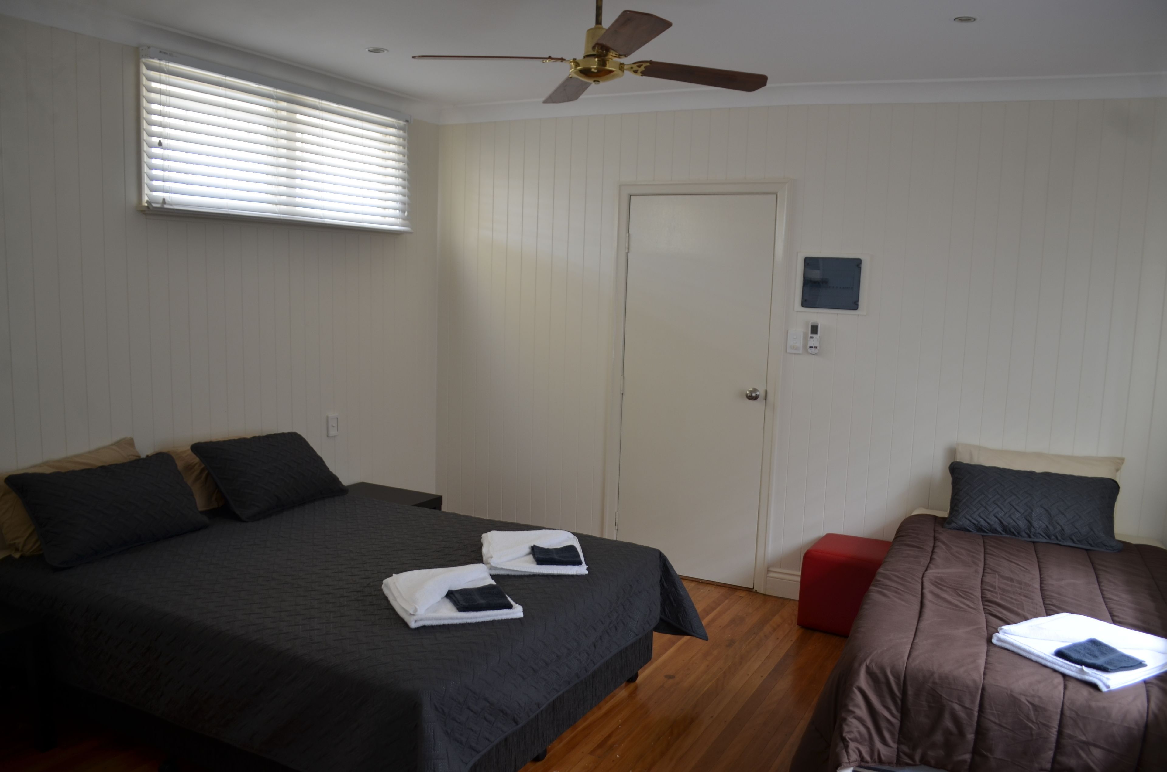 Habitación de hotel con dos camas, un ventilador de techo, una puerta y un ventanal pequeño.