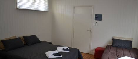 Habitación de hotel con dos camas, un ventilador de techo, una puerta y un ventanal pequeño.