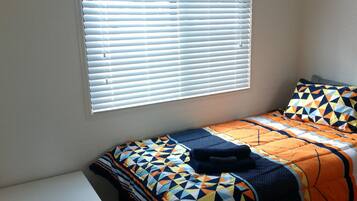 A single bed with a geometric patterned bedspread, a pillow, and a bedside table.