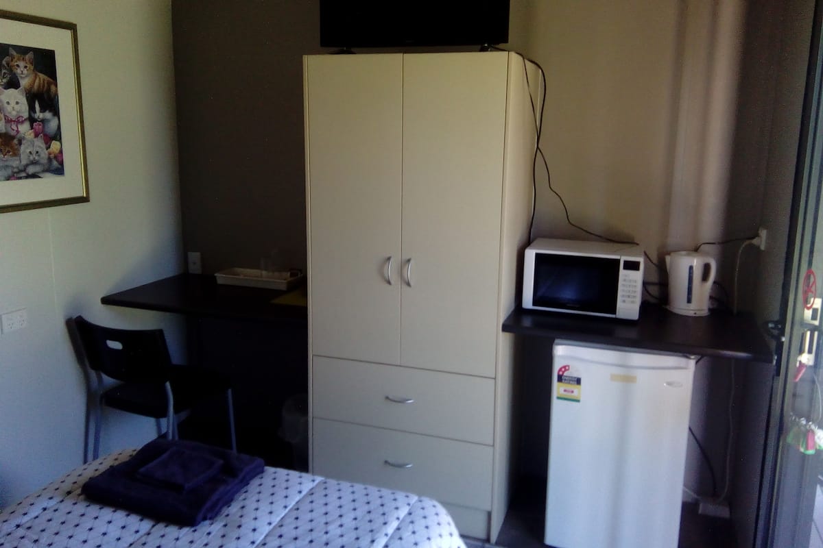Una habitación pequeña con cama, escritorio, armario, microondas y refrigerador.