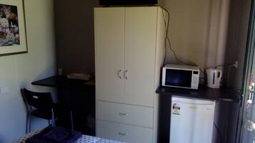 A small room with a bed, a desk, a cabinet, a microwave, and a refrigerator.