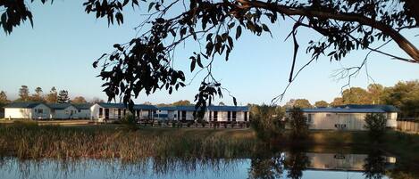 Un entorno tranquilo junto al lago, con una hilera de cabañas, cada una con un porche cubierto y una pequeña terraza.