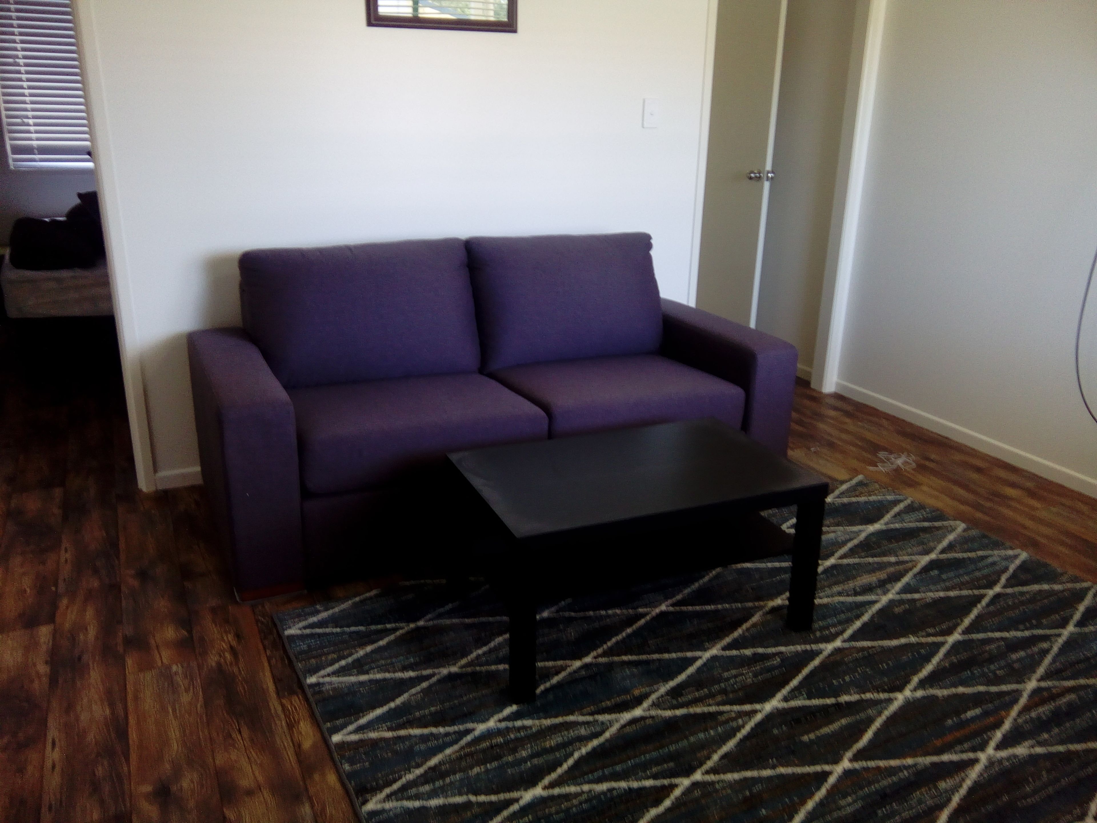 Uma sala de estar com um sofá roxo, uma mesa de centro preta e um tapete estampado.