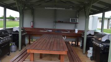 An outdoor covered picnic area with a wooden table, benches, a grill, and a microwave.