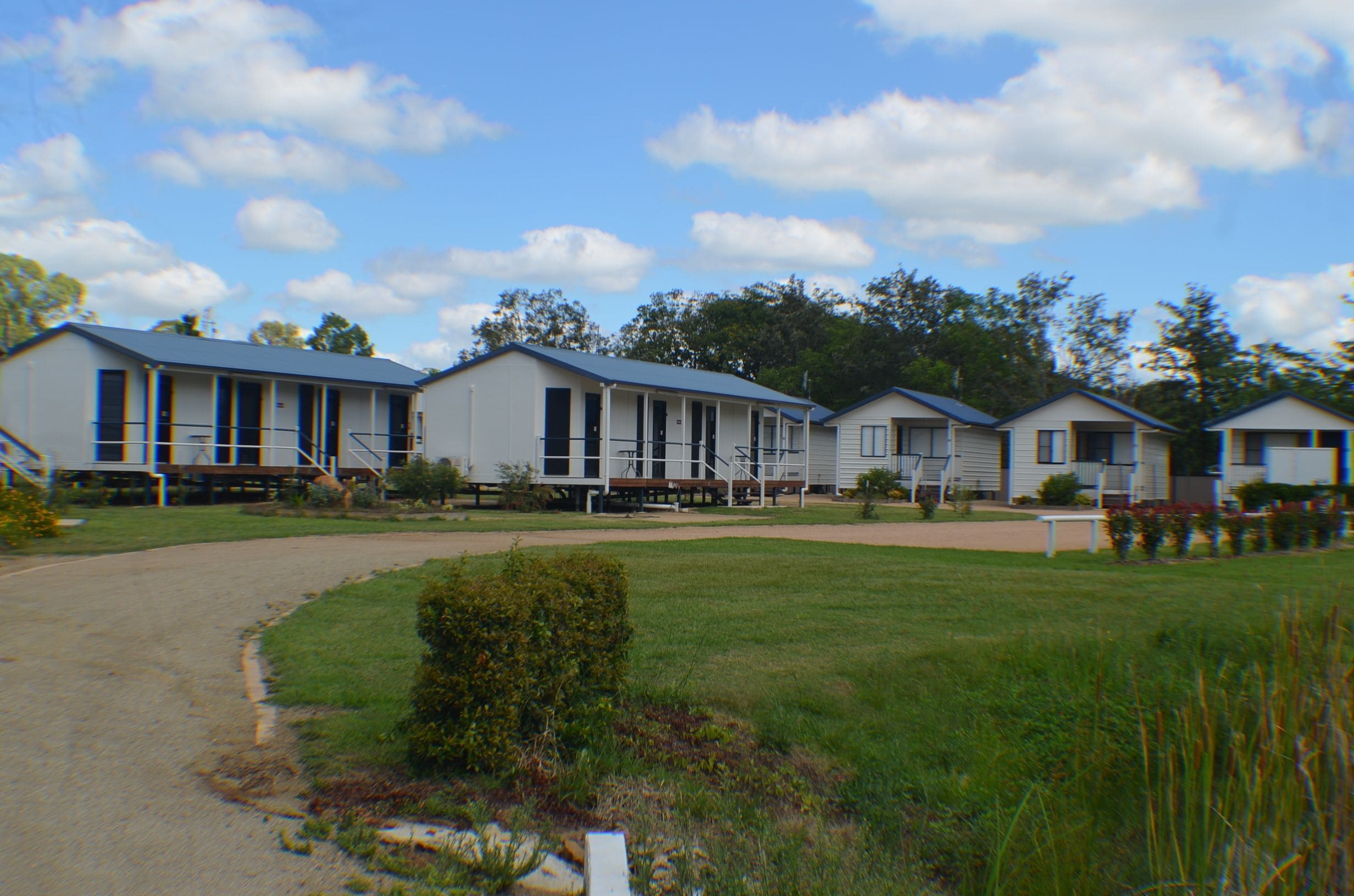 A row of single-story mobile homes with a paved driveway and grassy areas.