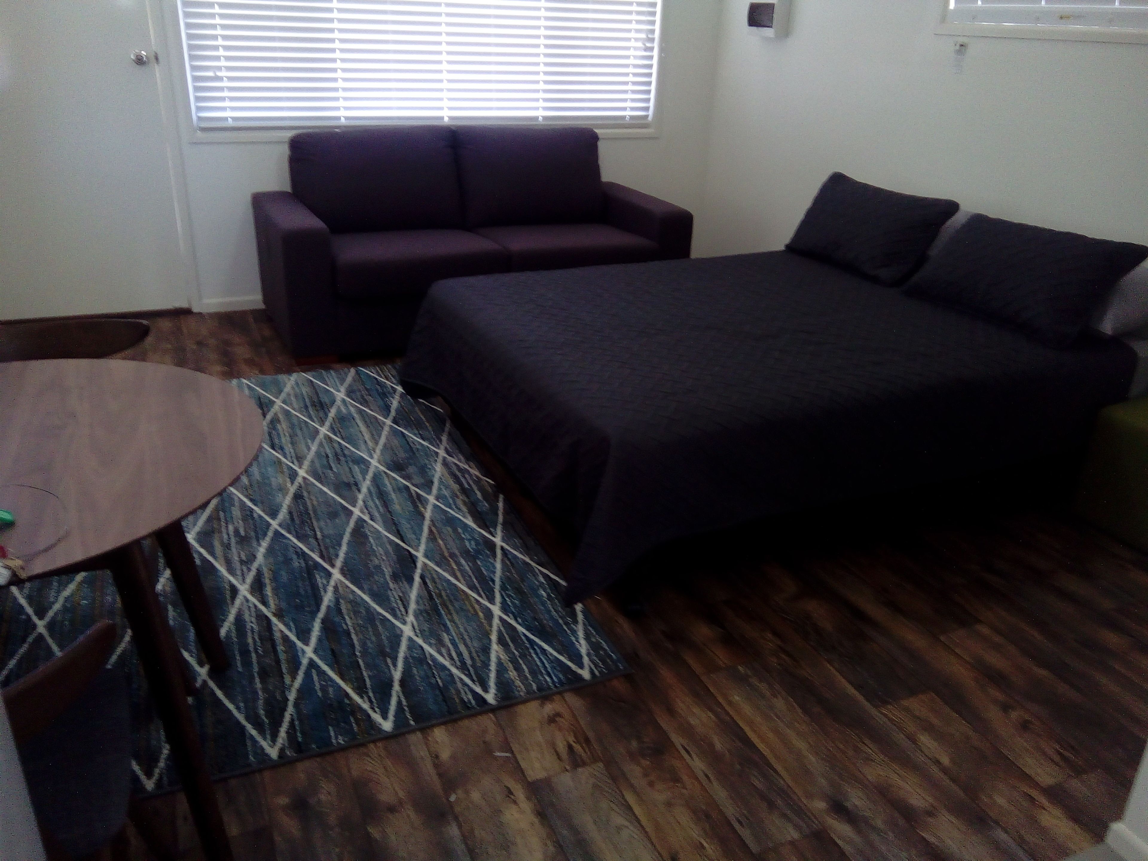 Una habitación pequeña con cama, sofá, una mesita y un tapete estampado.