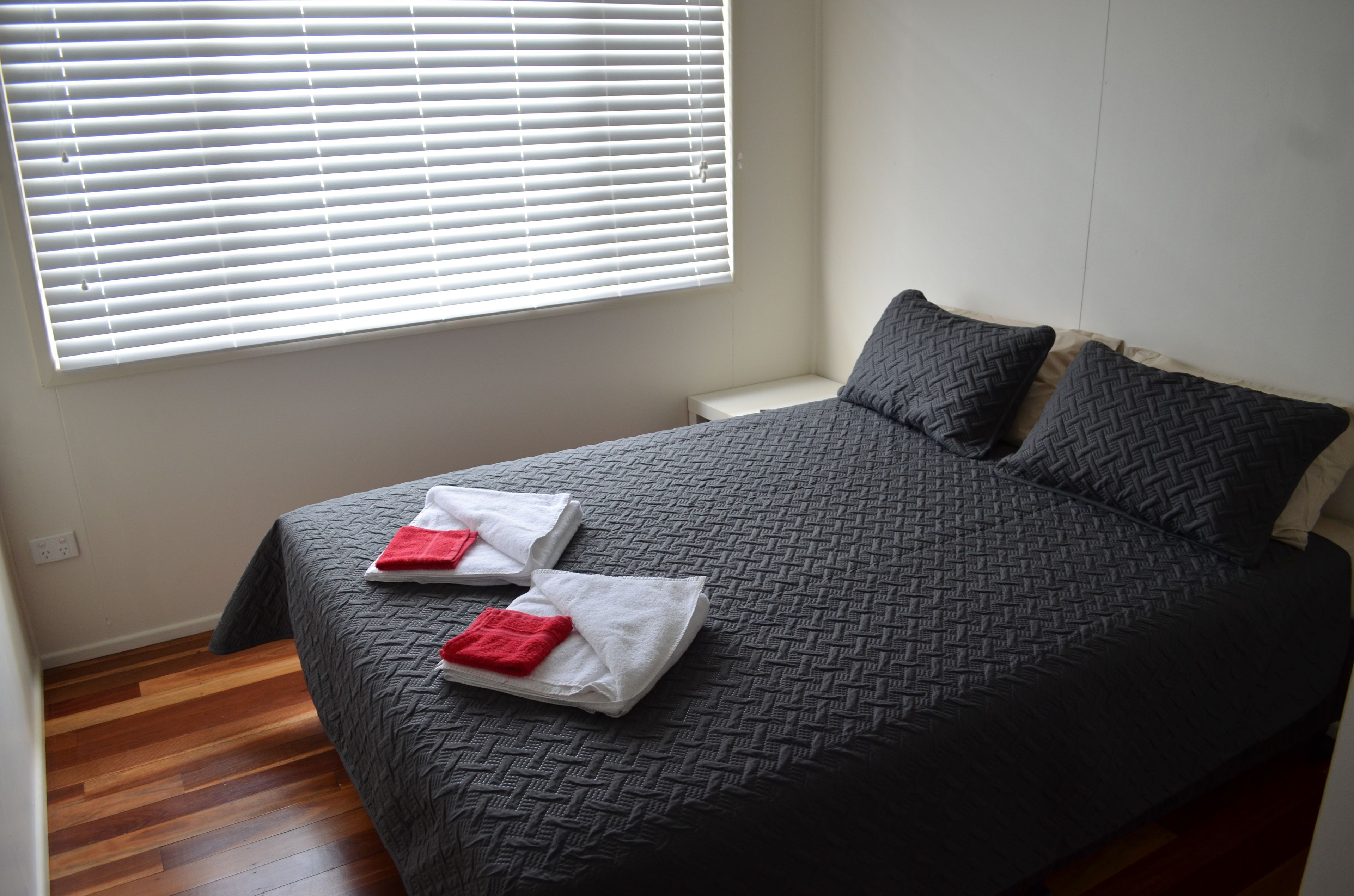 Un lit bien fait, recouvert d’une couverture à motifs sombres, avec deux oreillers et deux serviettes pliées posées sur le lit.