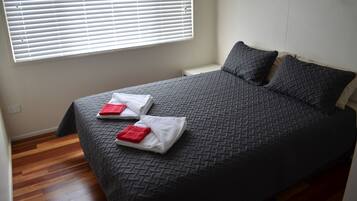 Un lit bien fait, recouvert d’une couverture à motifs sombres, avec deux oreillers et deux serviettes pliées posées sur le lit.