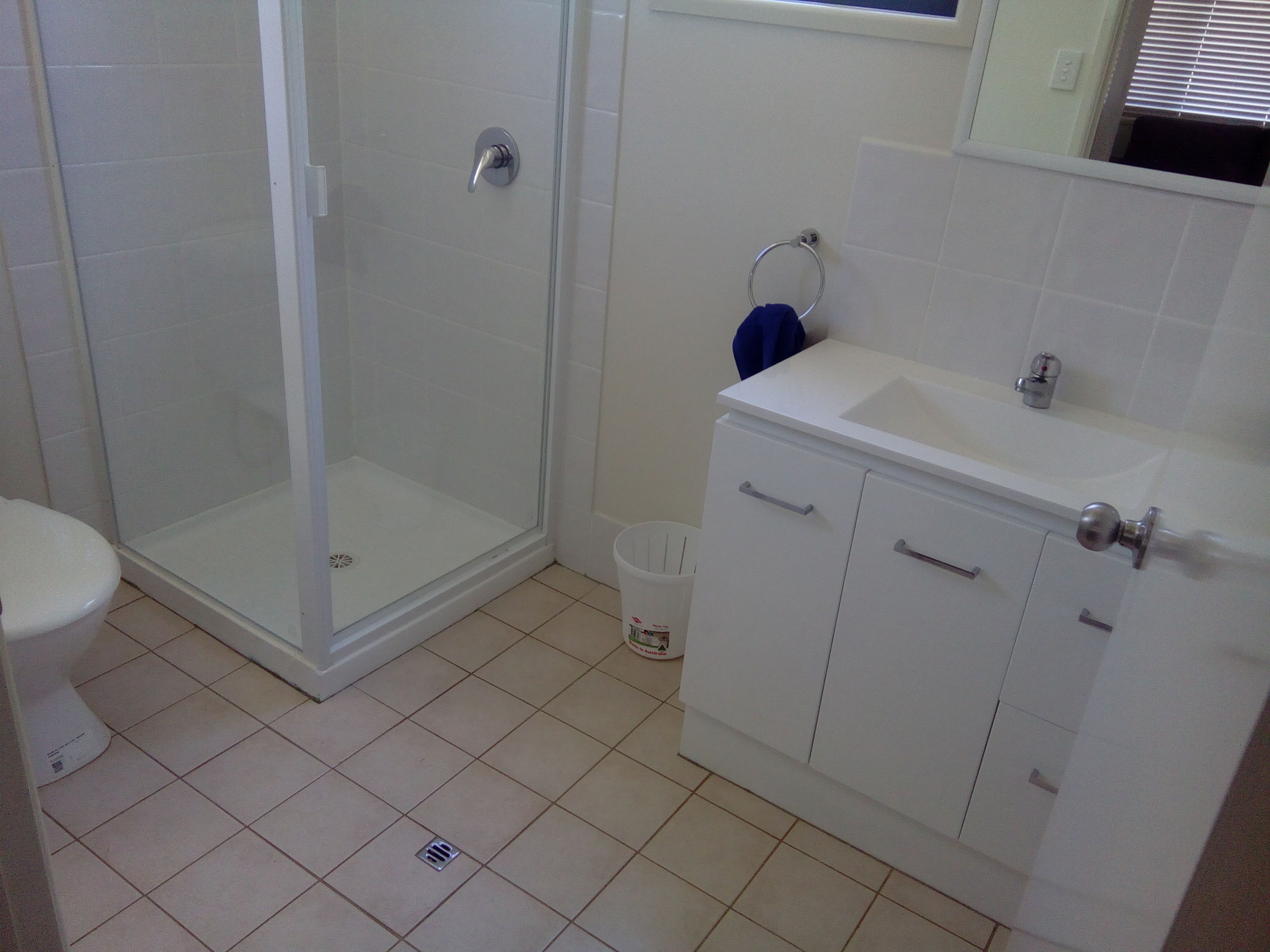Un baño con cabina de ducha de vidrio, un lavamanos blanco con espejo y un inodoro blanco.
