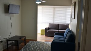 A living room with a sofa, a coffee table, and a TV mounted on the wall.