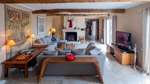 Ein großzügiges Wohnzimmer mit einer Couch, einem Couchtisch und einem Kamin. Im Raum befindet sich ein Fernseher und ein Bücherregal.