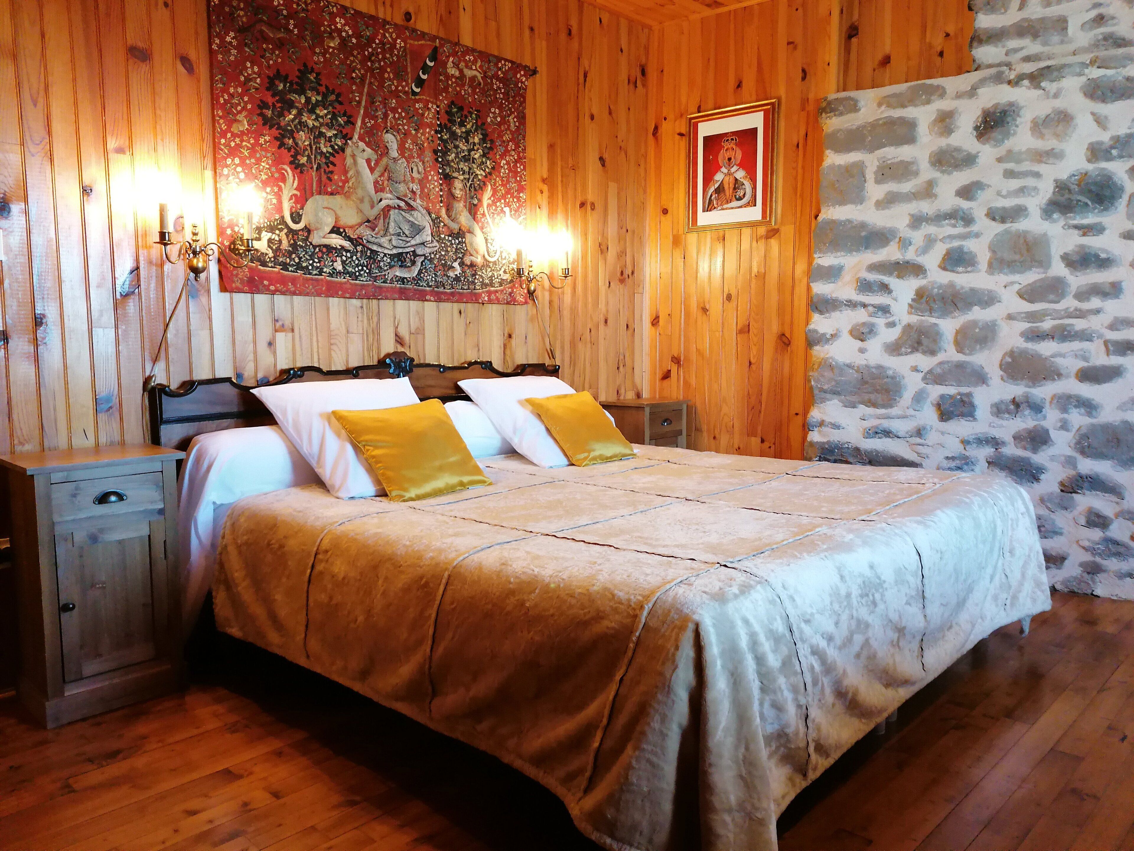 A wooden room with a bed, nightstands, a tapestry, and a stone wall.