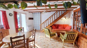 A cozy living room with a wooden staircase, a dining area with a round table, and a bookshelf. - Cottage in Anglards de Salers, beds made on arrival! (Anglards-De-Salers)