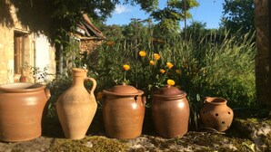 Five terracotta pots of varying shapes and sizes placed on a stone surface outdoors, with a rustic house and greenery in the background. - Cottage rental Les tilleuls stone house in Perigord Noir Sarlat (Castels)