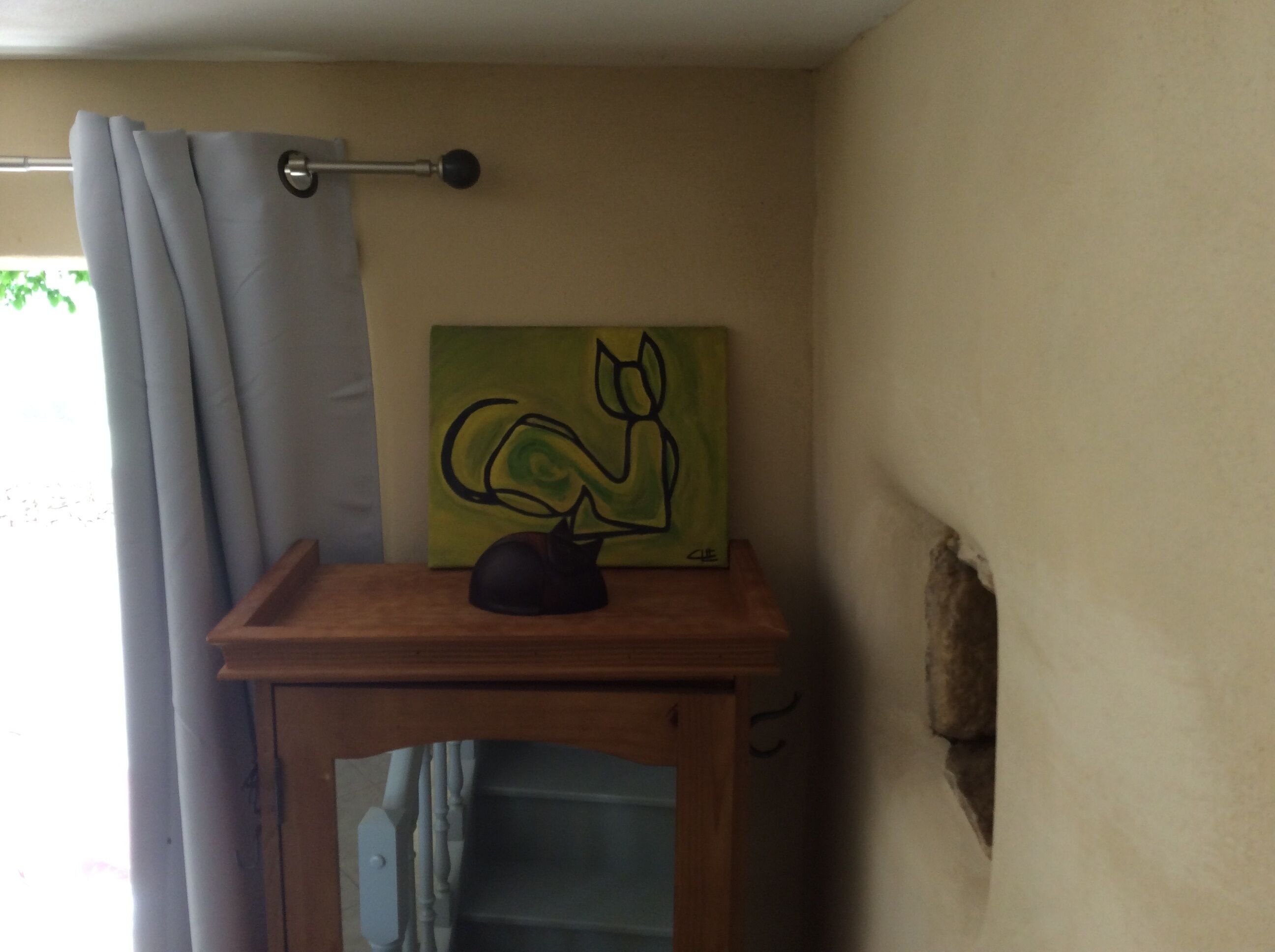 Ein Badezimmer mit hölzernem Waschtisch, einem abstrakten grünen Gemälde, einer schwarzen Katzenfigur und einem Handtuchhalter.