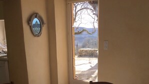 A dining area with a round table covered by a polka dot tablecloth, a chair with a heart-shaped backrest, and a view of a stone wall and trees through a glass door. - Cottage rental Les tilleuls stone house in Perigord Noir Sarlat (Castels)