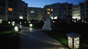 A pathway leading to a building with multiple balconies and windows, surrounded by well-lit garden areas and decorative lighting. - B&B Cote d'azur, Your seaside holiday in Hammamet.<br> (Hammamet)