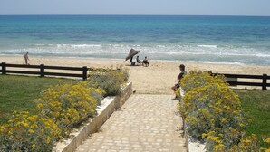 A beach with a paved walkway leading to the shore, bordered by yellow flowers and a wooden fence. - B&B Cote d'azur, Your seaside holiday in Hammamet.<br> (Hammamet)