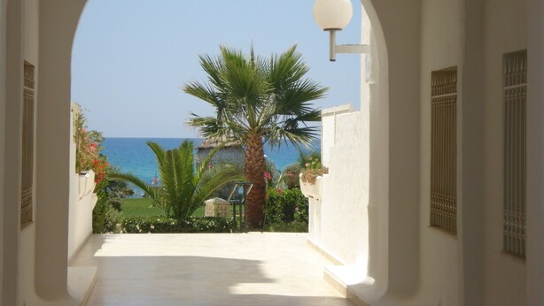 A corridor with a view of the sea, palm trees, and a building with a thatched roof. - B&B Cote d'azur, Your seaside holiday in Hammamet.<br> (Hammamet)