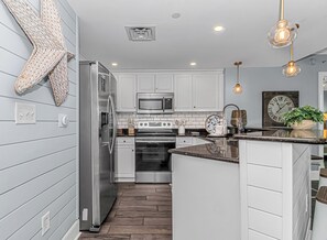 A modern kitchen with stainless steel appliances, white cabinetry, and a wooden floor. - Blue Haven · Direct Oceanfront 3BR, Sleeps 10, High Floor (North Myrtle Beach)