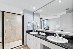 A modern bathroom with two sinks, a large mirror, and a glass shower enclosure. - Blue Haven- Ocean Front Condo at Mar Vista Grande Summer Specials Available! (North Myrtle Beach)