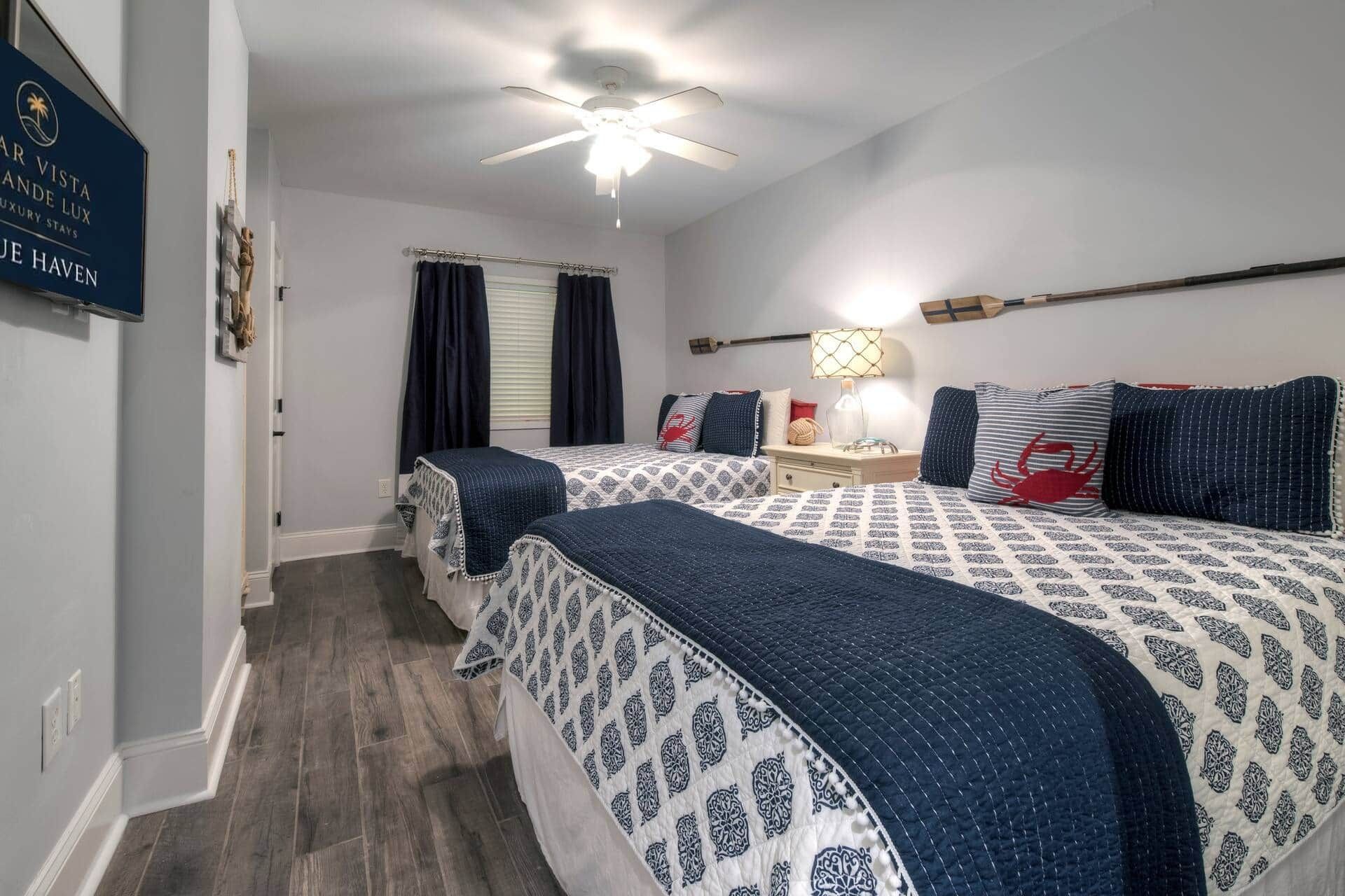 Une chambre d’hôtel avec deux lits, un ventilateur de plafond, une table de chevet avec une lampe et un téléviseur fixé au mur.