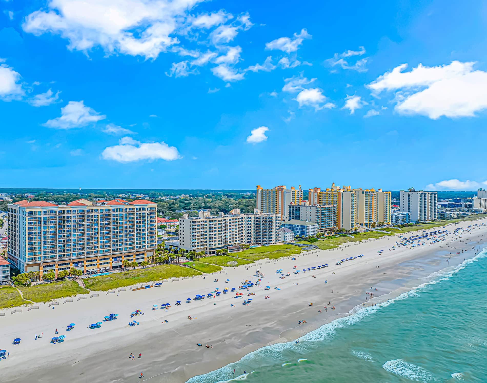 A coastal cityscape with a wide beach, high-rise hotels, and clear skies.