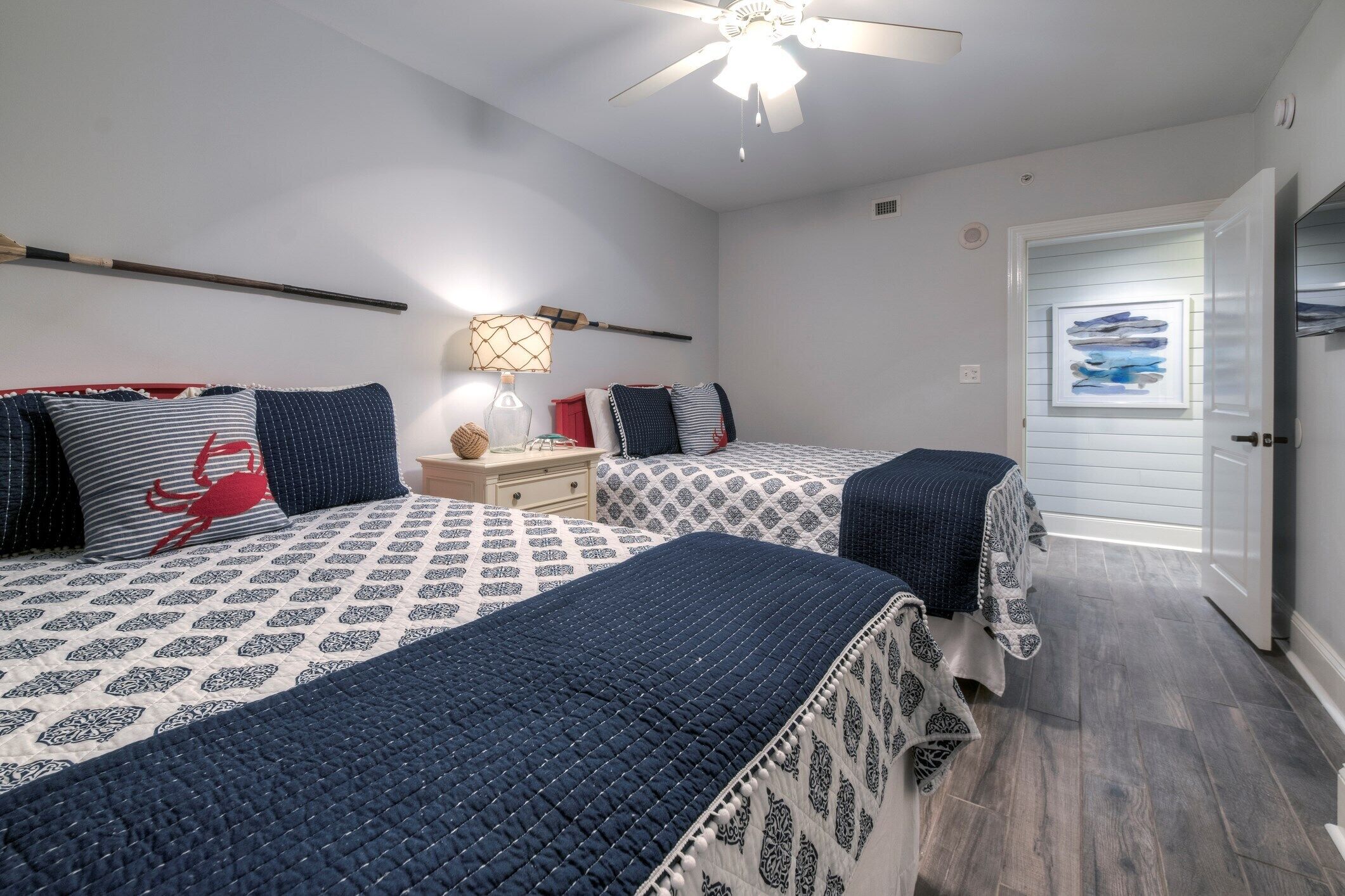 Une chambre avec deux lits, une table de chevet, une lampe et un ventilateur de plafond.