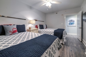 A bedroom with two beds, a nightstand, a lamp, and a ceiling fan.