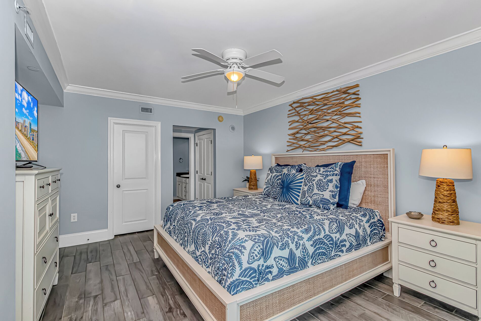 A bedroom with a bed, a ceiling fan, a wall-mounted lamp, and a door leading to another room.