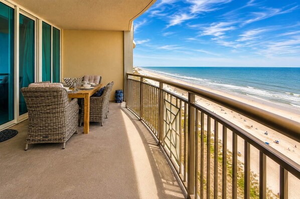 A balcony with wicker furniture and a view of the beach.
