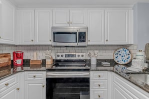 Una cocina con armarios blancos, un microondas de acero inoxidable, un horno Samsung y una cafetera.