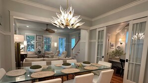 A modern dining area with a glass table, white chairs, and a unique chandelier. - "The Lighthouse" in WaterColor. Pool, Walk to beach, 4 Bikes & WC amenities incl (Santa Rosa Beach)