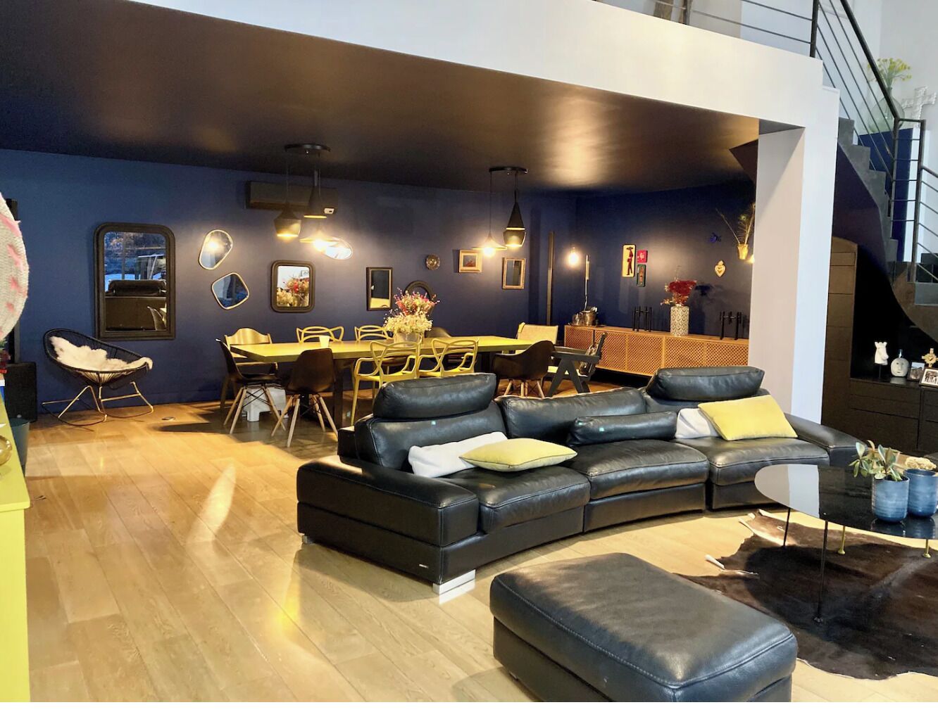 A modern living room with a sectional sofa, a dining area, and a staircase.