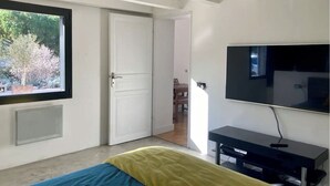 Un dormitorio con cama, televisión, ventana y puerta que da a otra habitación.