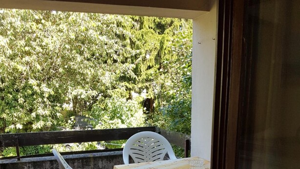 A balcony with a table and chairs, a view of trees, and a tiled floor. - Pension Streng-Reinhardt (Ostfildern)