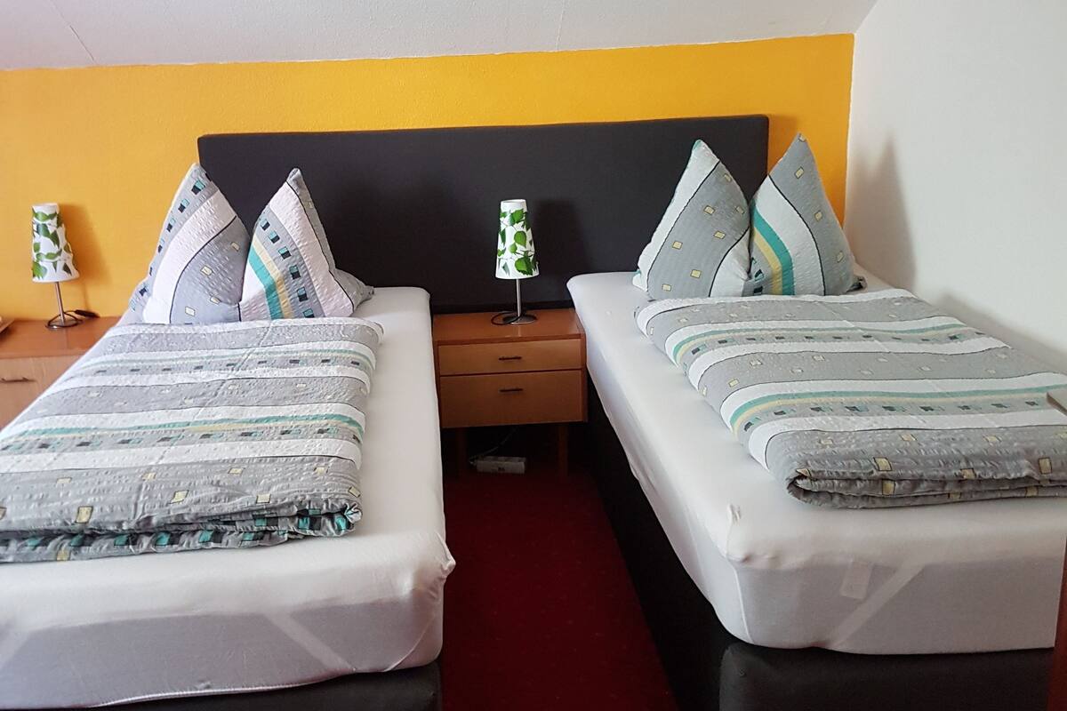 Ein Hotelzimmer mit zwei Betten, jeweils mit einem schwarzen Kopfteil, einem roten Teppich und einem kleinen Tisch mit einer Lampe dazwischen.