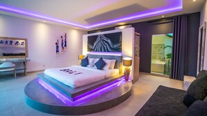 A modern bedroom with a curved bed, ambient lighting, a large artwork, and a view of the bathroom. - Exclusive Private 8 Bedroom Estate, 2 Huge Pools, Seminyak (Seminyak)