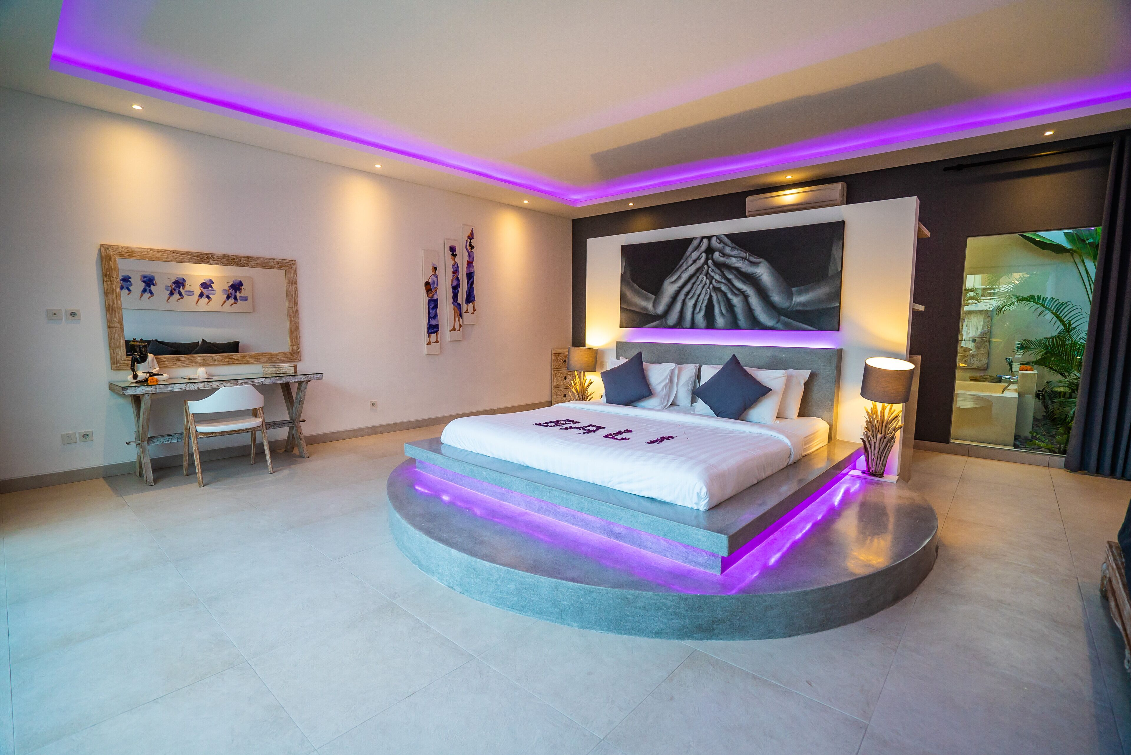 A modern bedroom with a bed centered on a circular platform, a desk with a chair, and artwork on the walls.